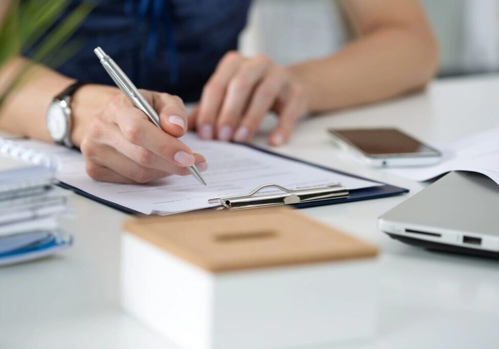 Person writing on clipboard at desk.