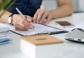Person writing on clipboard at desk.