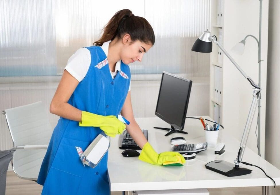 Woman cleaning office desk with computer.