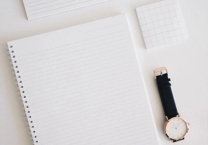 Notebook, watch, planner, and notepad on desk.