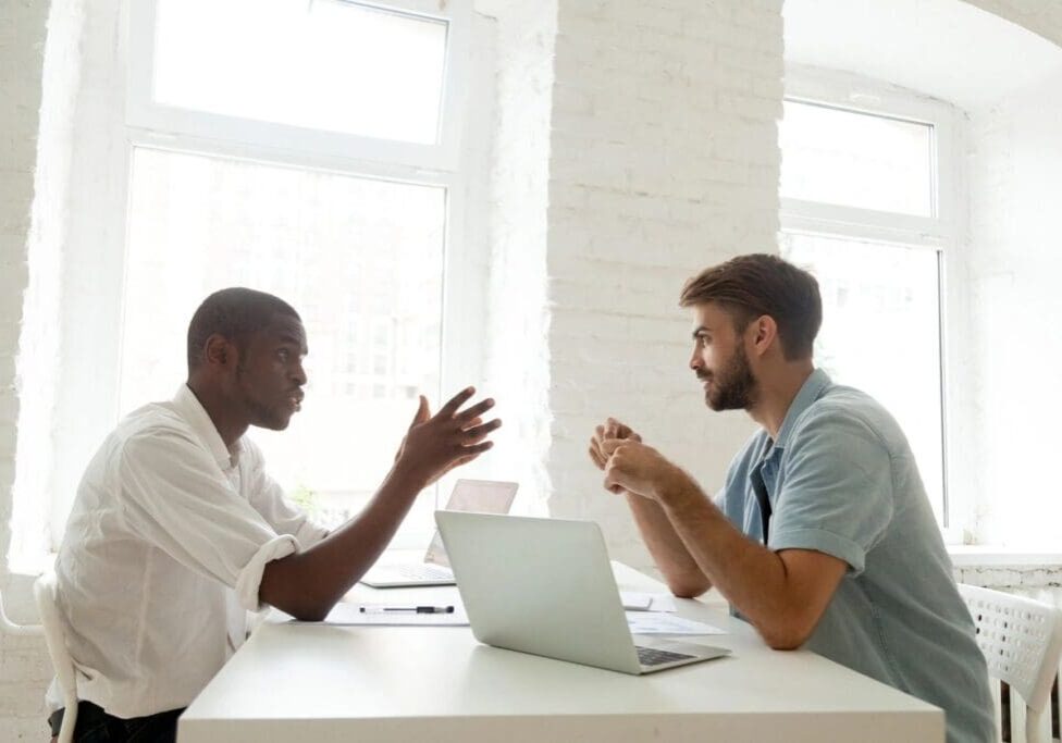 Two men discussing work at desk.