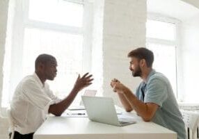 Two men discussing work at desk.