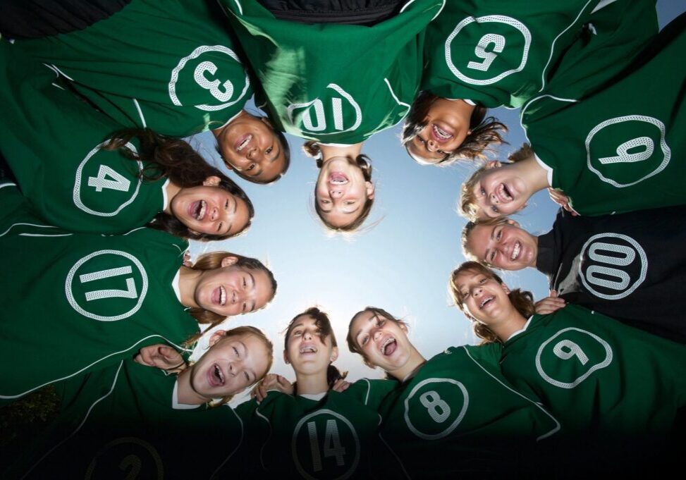 Sports team huddle in green uniforms, smiling.