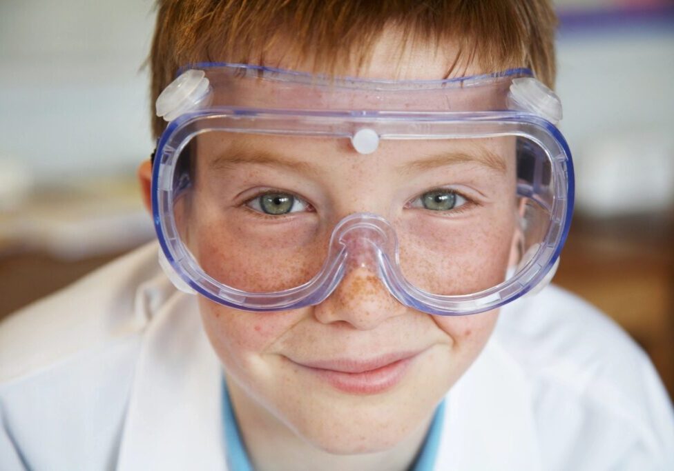 Child wearing safety goggles in lab coat.